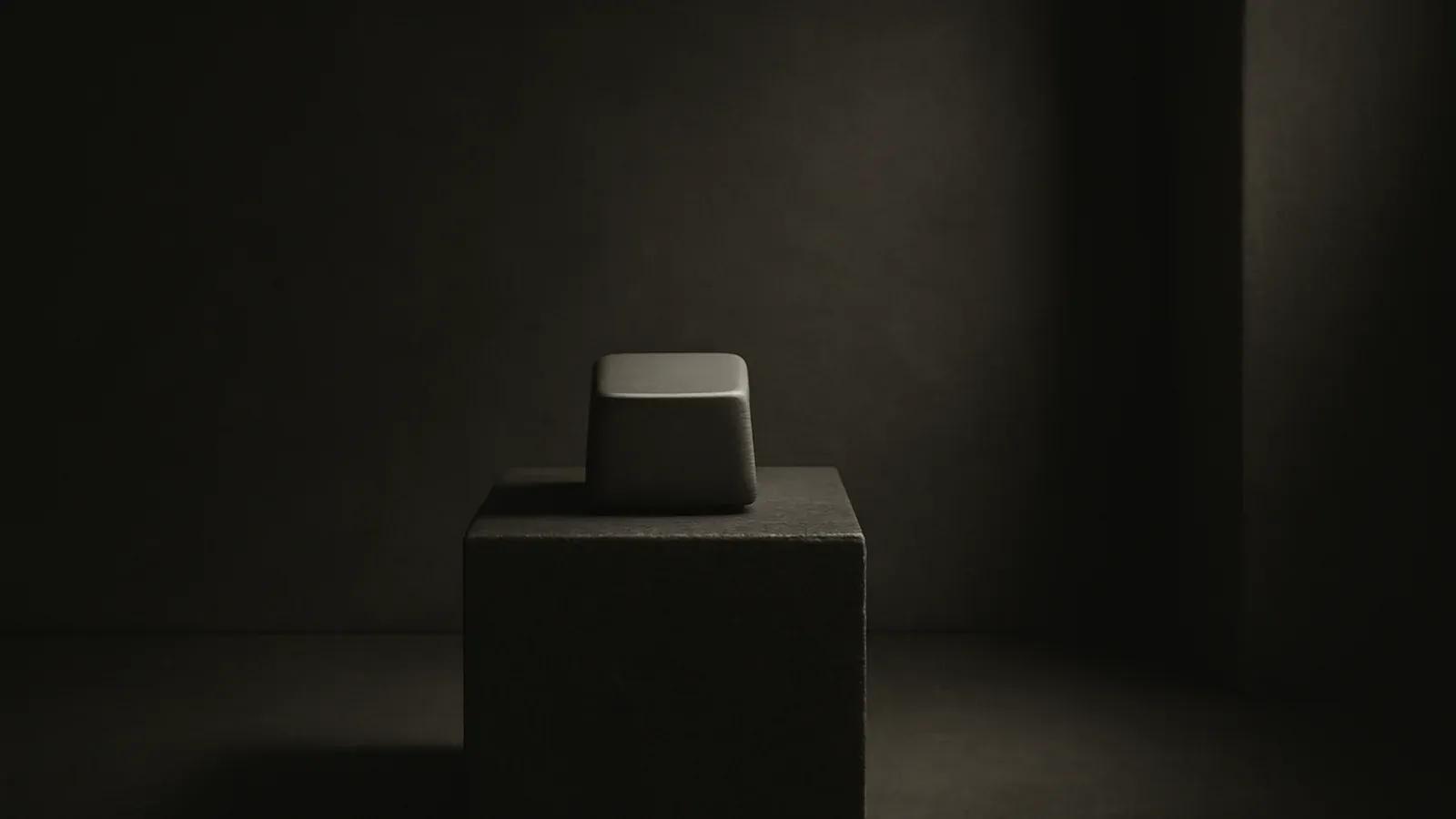 A dark stone plinth holding a single blank keyboard key, lit from one side, its surface worn smooth from use.