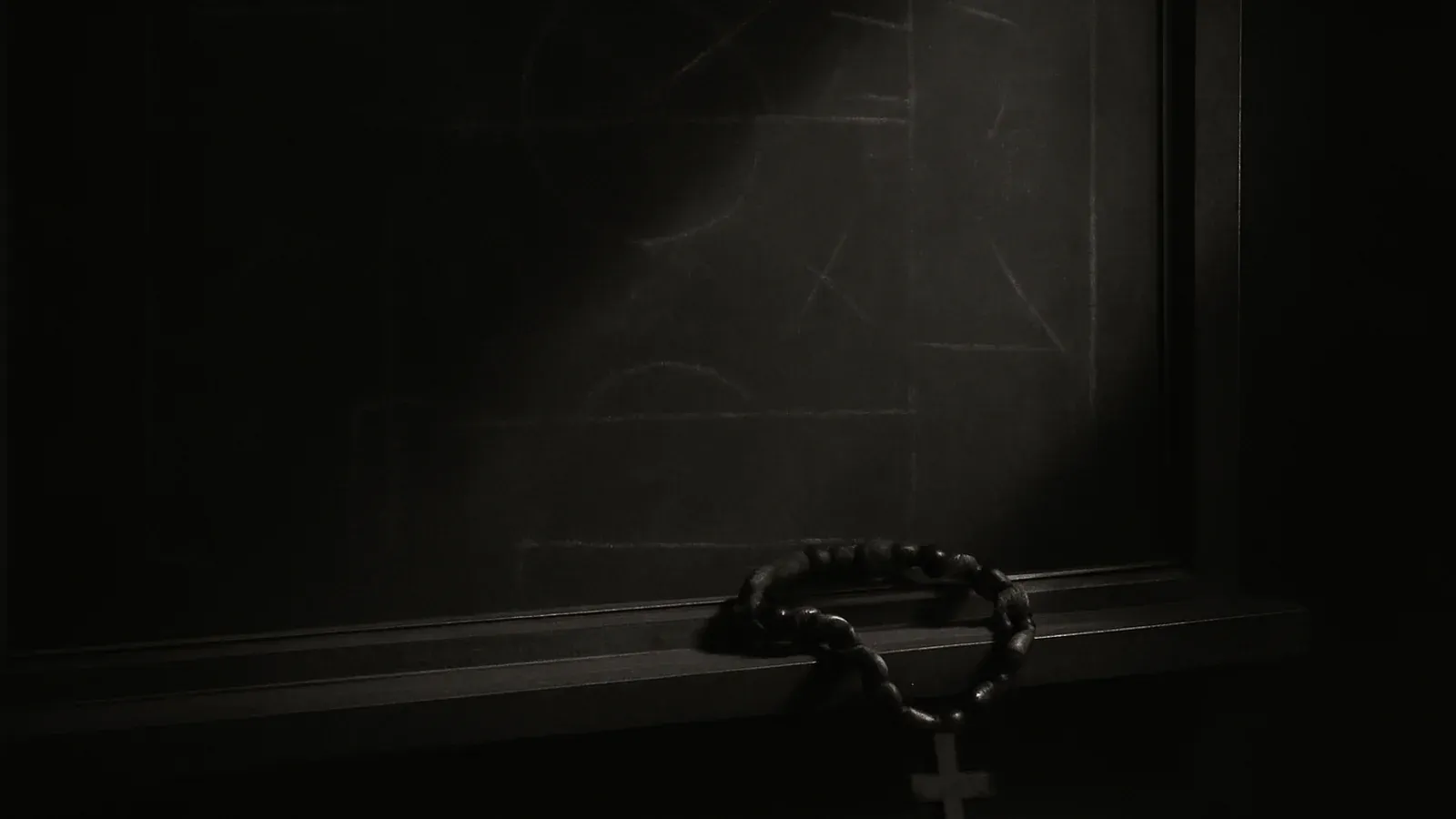 A wooden rosary resting on the ledge of an old slate tactics board, lit by a single shaft of light.