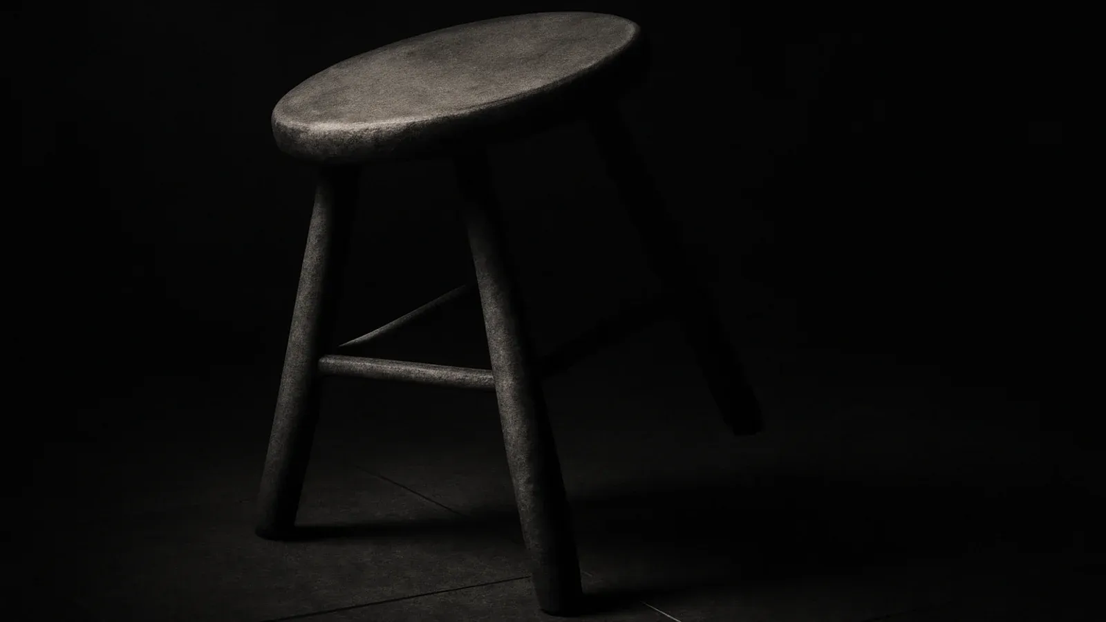A weathered three-legged wooden stool tipped off balance in raking light, its weight riding on a single planted leg while the others hang short of the stone floor.