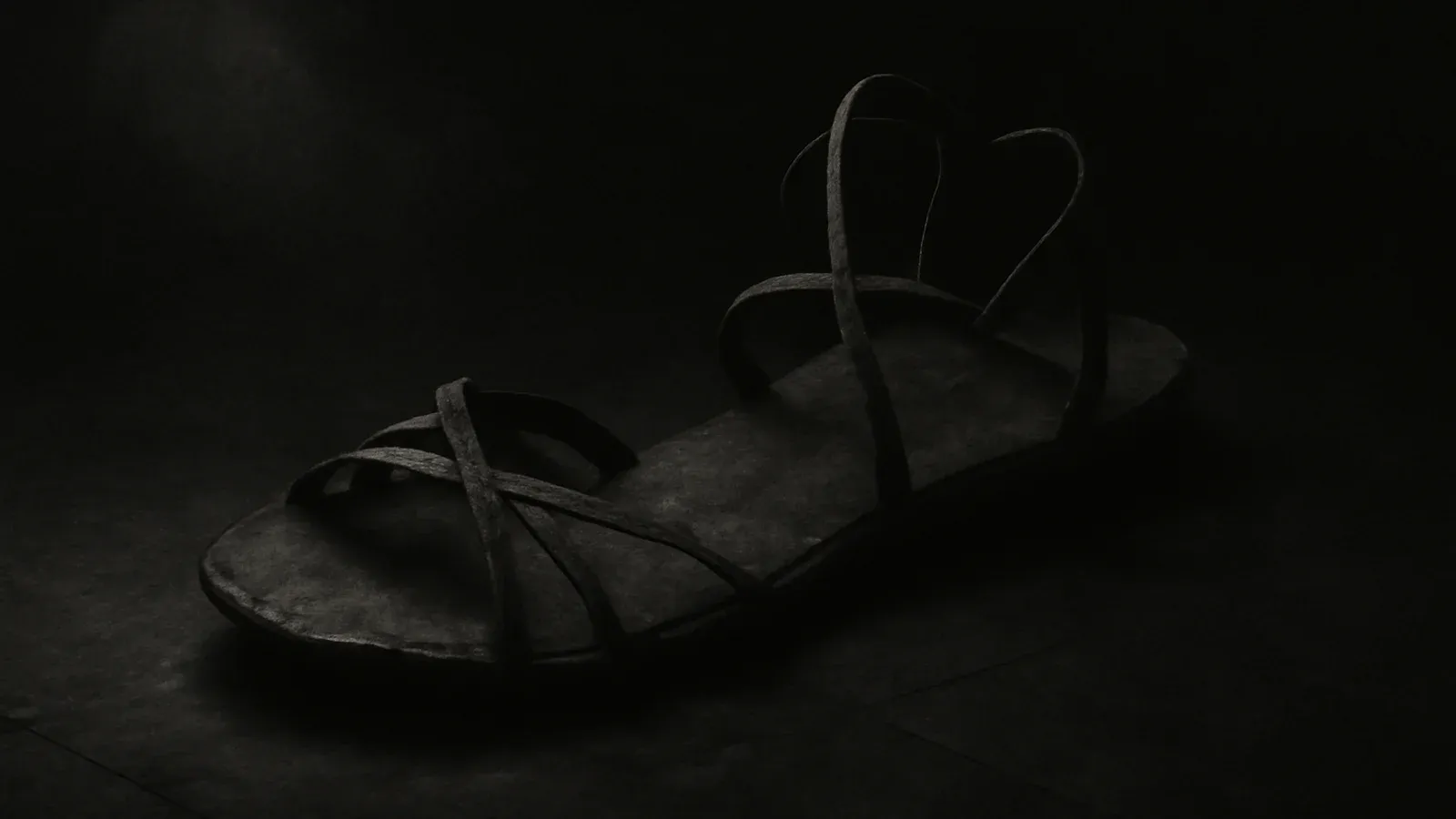 A single worn ancient leather sandal on a dark stone floor under a soft shaft of light.